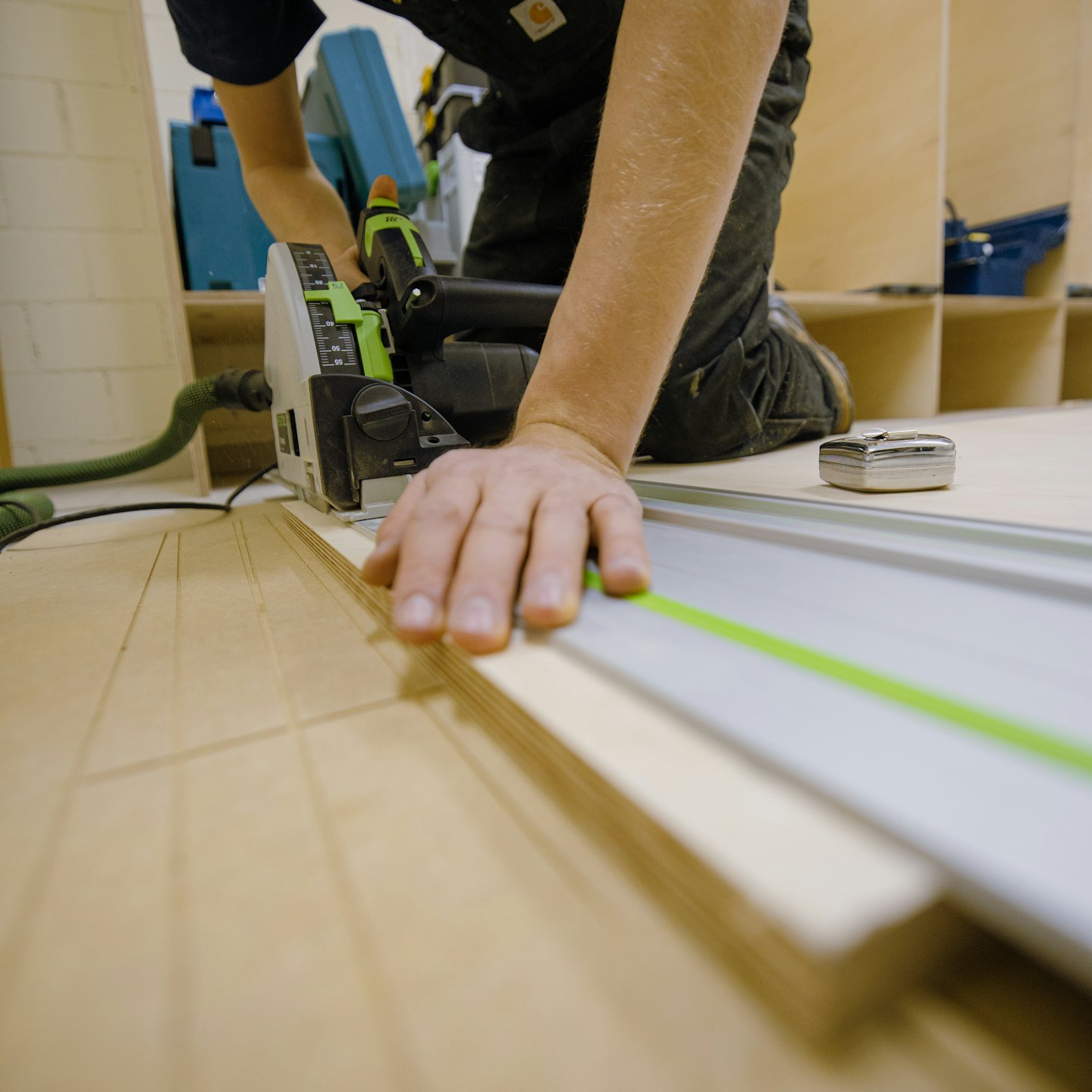 Hands guiding a track saw to cut plywood in a workshop.